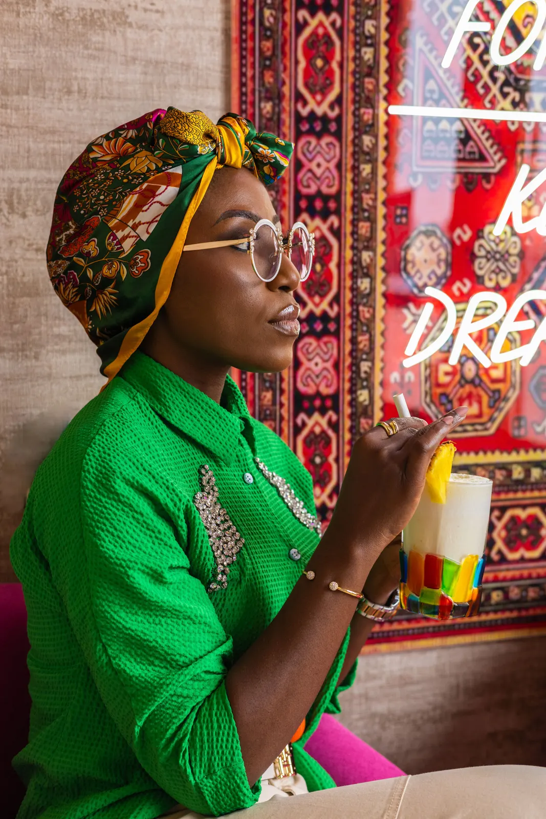Azeezat in a green shirt and head wrap, sipping a drink