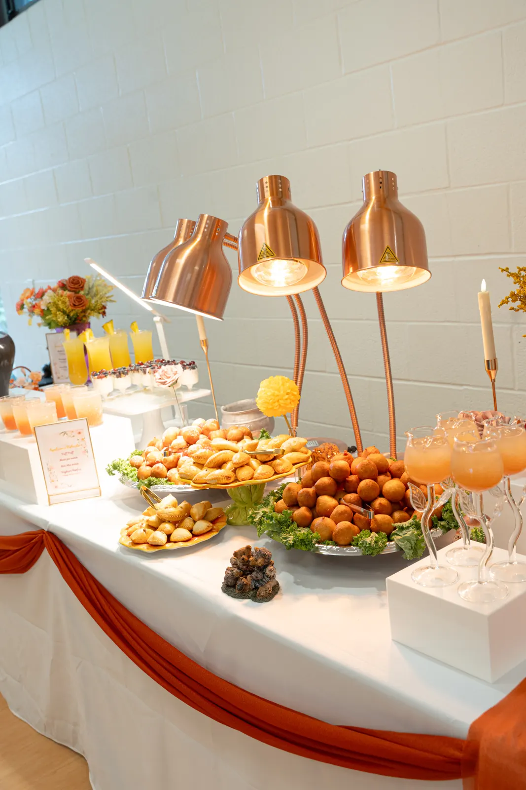 A TFL event table with pastries, small chops and drinks under copper food lamps